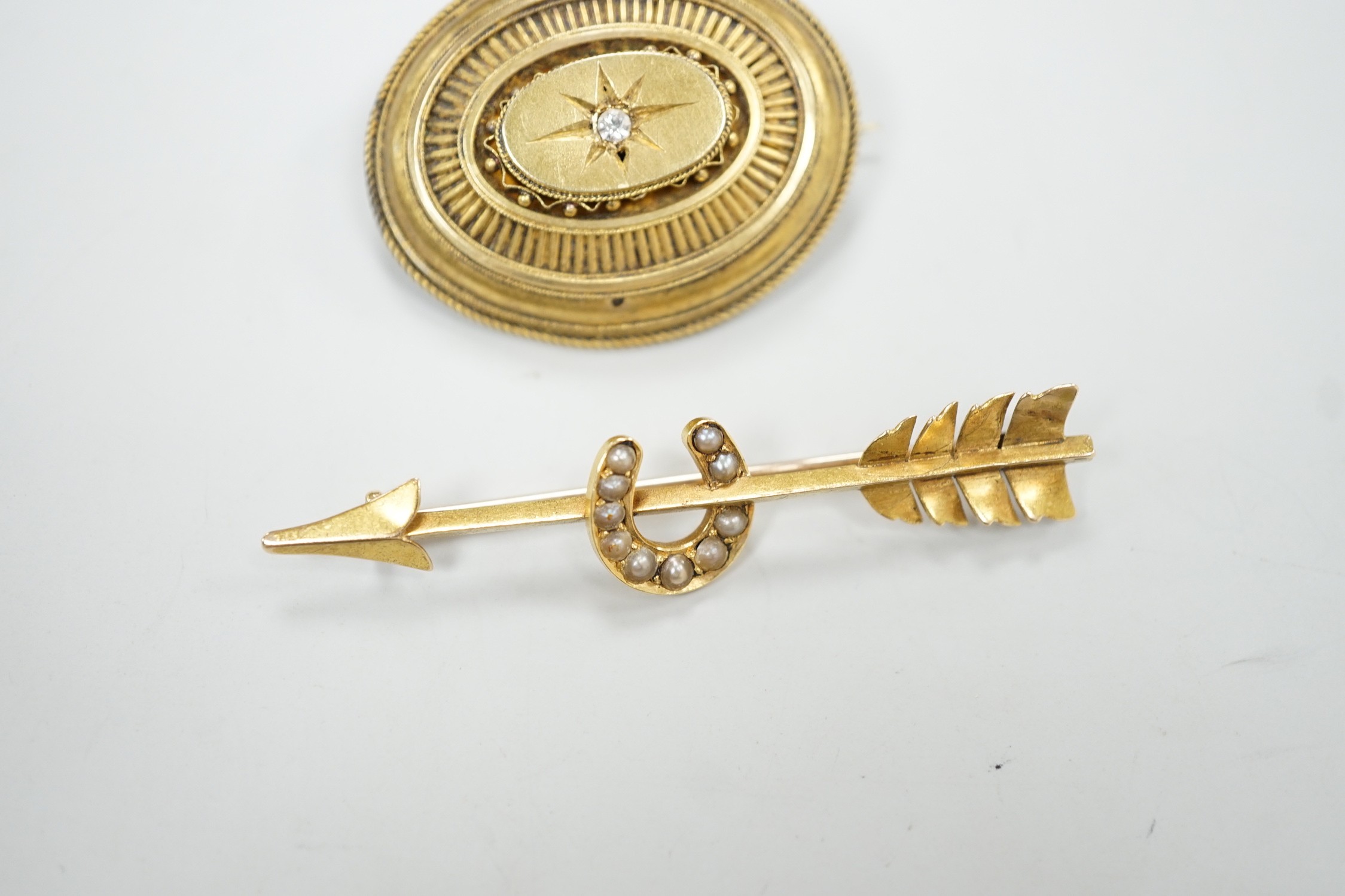 An early 20th century yellow metal, and seed pearl set arrow and horse shoe brooch, 60mm and a Victorian paste set yellow metal oval brooch.